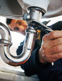 Close-up of plumber repairing sink. Male worker using tool while fixing appliance in bathroom. He is working on metallic equipment at home.