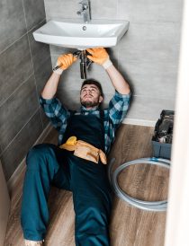 handsome repairman fixing water damage with adjustable wrench in bathroom